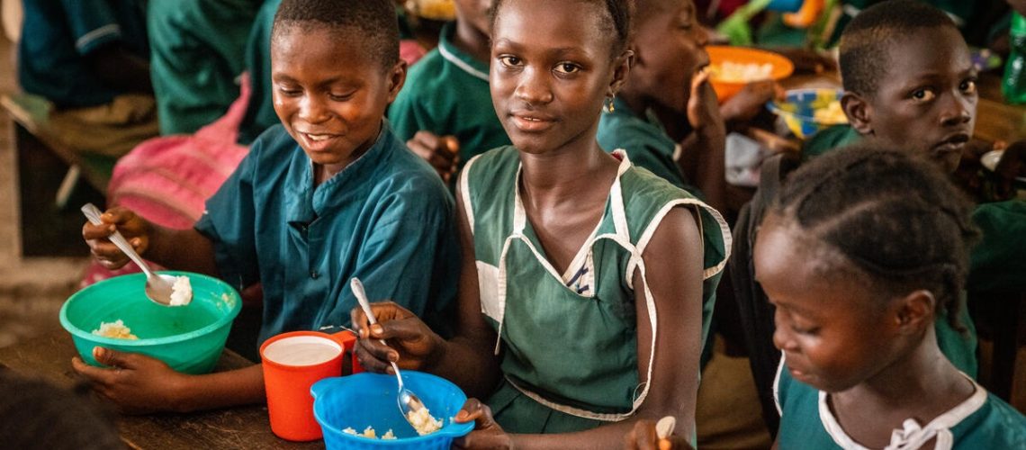 Students at KDC Primary School in Dar Es Salaam Community, Sierra Leone enjoying a hot  meal of rice and vegetables provided by the WFP supported school feeding program.

On request from the Government, the World Food Programme implements school feeding in Sierra Leone, reaching over 216,000 children in 970 primary and pre-primary schools (as at May 2022). WFP provides one mid-morning hot meal per child per day, its food basket comprising of cereals, pulses, fortified vegetable oil and iodized salt.

WFP’s assistance is intended to draw children to school, enable their learning and improve attendance and completion rates.

In addition to providing food, as well as cooking items in some schools, WFP trains school staff in hygiene and stores and commodity management for accountability and food safety.